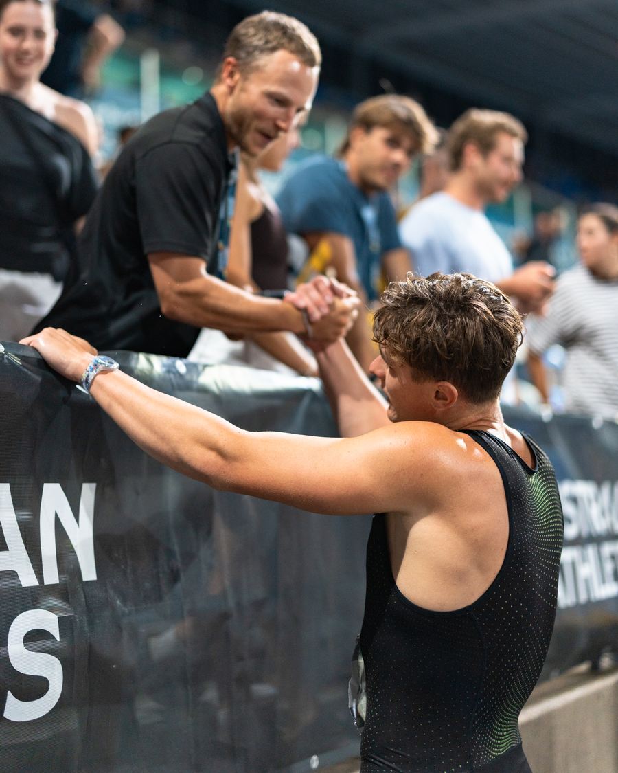 A coach reaching over the barrier to shake an athlete's hand after a race.